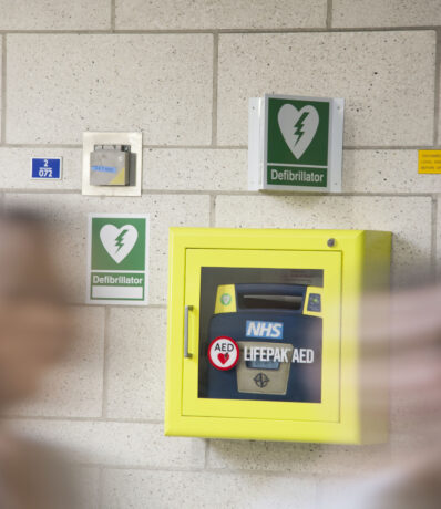 A Defibrillator attached to a wall in a yellow cabinet