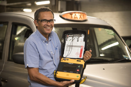 Cabbie Paul in front of his taxi holding his defibrillator