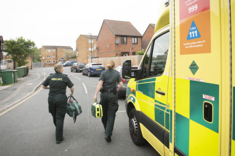 A photograph of an ambulance with two female medics in green uniform walking away carrying kit bags