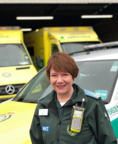 Debbie stood in front of an ambulance car and two ambulances in her green Service uniform