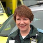 Debbie in uniform in front of ambulance vehicles