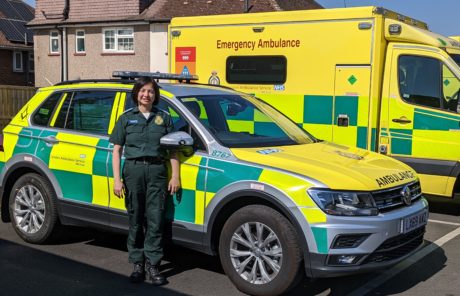 Mina stands in uniform in front of an ER response car and an ambulance