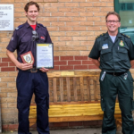 Nick holds his certificate in front of bench with two paramedics and a firefighter