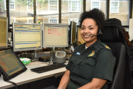 A female call handler sat at a desk with a headset and computer screens in background