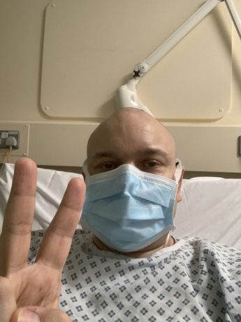 Richard in hospital with mask giving victory sign