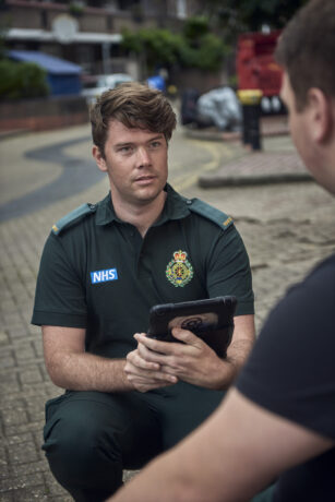 A paramedic with an iPad knelt speaking to a patient