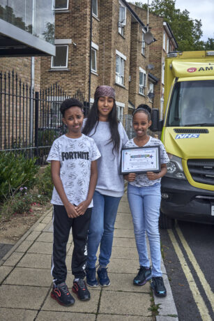 Rawda holds her certificate alongside her mum and brother in front of ambulance