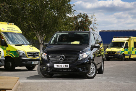 A black mercedes van in a car park with ambulances