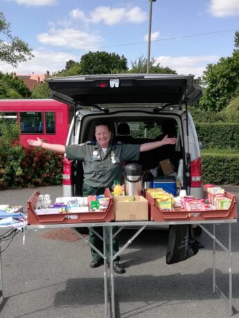 A medic posing in front of a tea truck with a table of food and drink