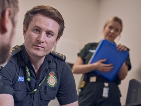 A paramedic speaks to a patient while a mental health nurses watches on