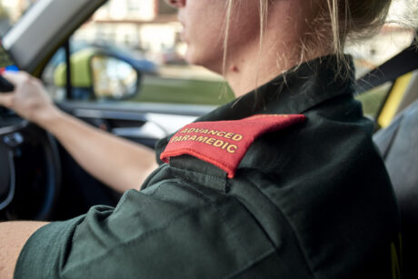 Medic shown in ambulance cab and her epaulettes which read Advanced Paramedic are visible in foreground