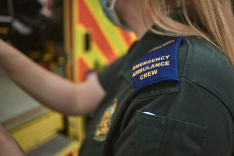 A medic shown behind an ambulance with her epaulettes which read Emergency ambulance Crew visible