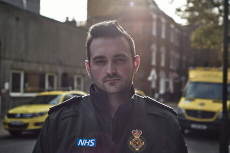 Kieran stands with an ambulance car and ambulance behind him