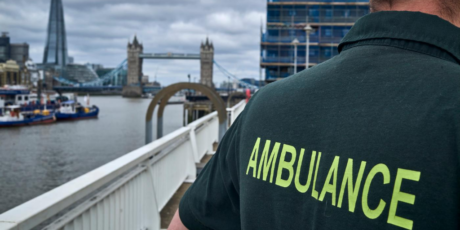 Medic shown from behind with the word Ambulance on their top visible and with Tower Bridge in the background