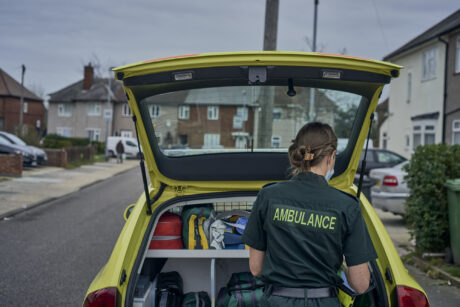 A female medic photographed from behind as she gets equipment from an ambulance car's open boot