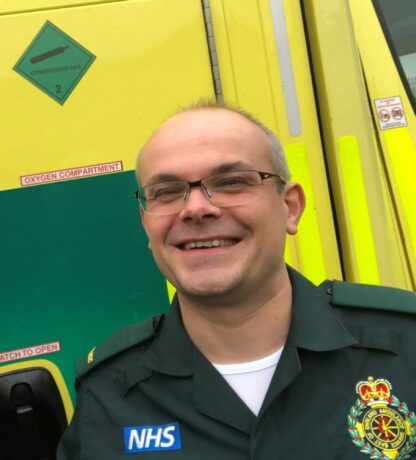 Dr Martin in ambulance uniform stood in front of the side of an ambulance