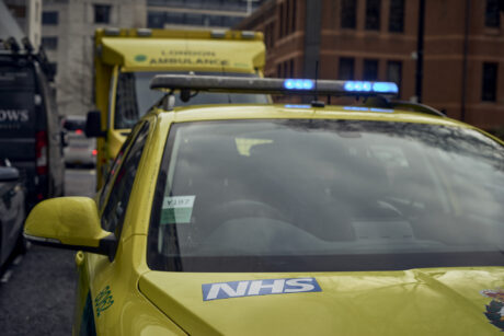 An ambulance car with blue lights flashing parked in front of an ambulance