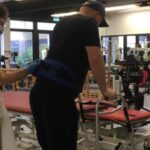 Sean with the help of a nurse walks with a Zimmer frame in hospital