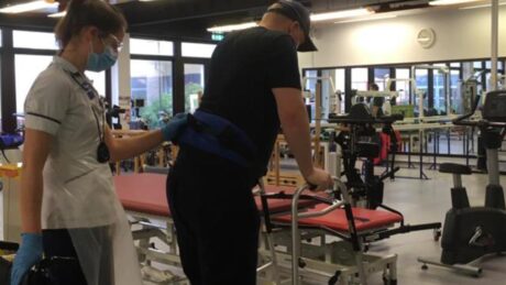 Sean with the help of a nurse walks with a Zimmer frame in hospital