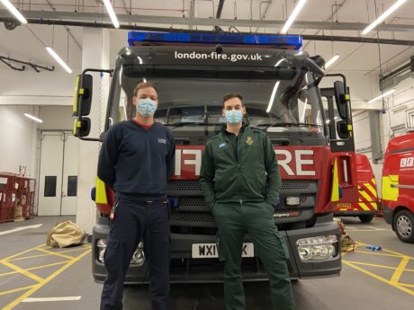 Firefighter Reece and Paramedic Alex standing in their uniforms in front of a fire engine