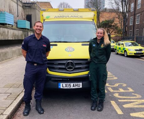 Olly and Caitlin stood in front of an ambulance either side of the bonnet