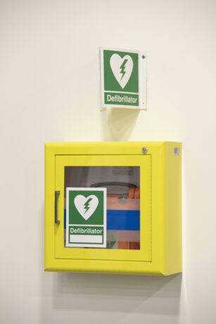 A defibrillator in a yellow cabinet attached to a wall