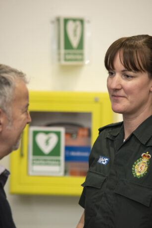 A LAS medic in uniform speaks to a man in front of a defibrillator cabinet