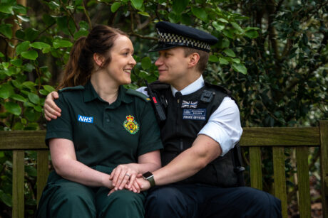 Paige and Rob photographed on a bench in uniform and Rob has his arm around Paige