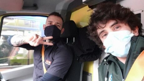 Jason and Matthew wearing masks and smiling for the camera in their respective Service uniforms in an ambulance cab