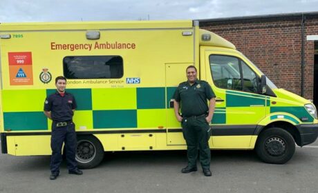 Uzair and Obi in their firefighter and paramedic uniforms stood in front of an ambulance