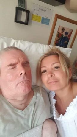 Paul lying in a hospital bed with Ellie by his side