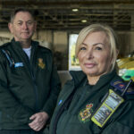 Dave and Ellie stood in LAS uniform in front of a row of ambulances