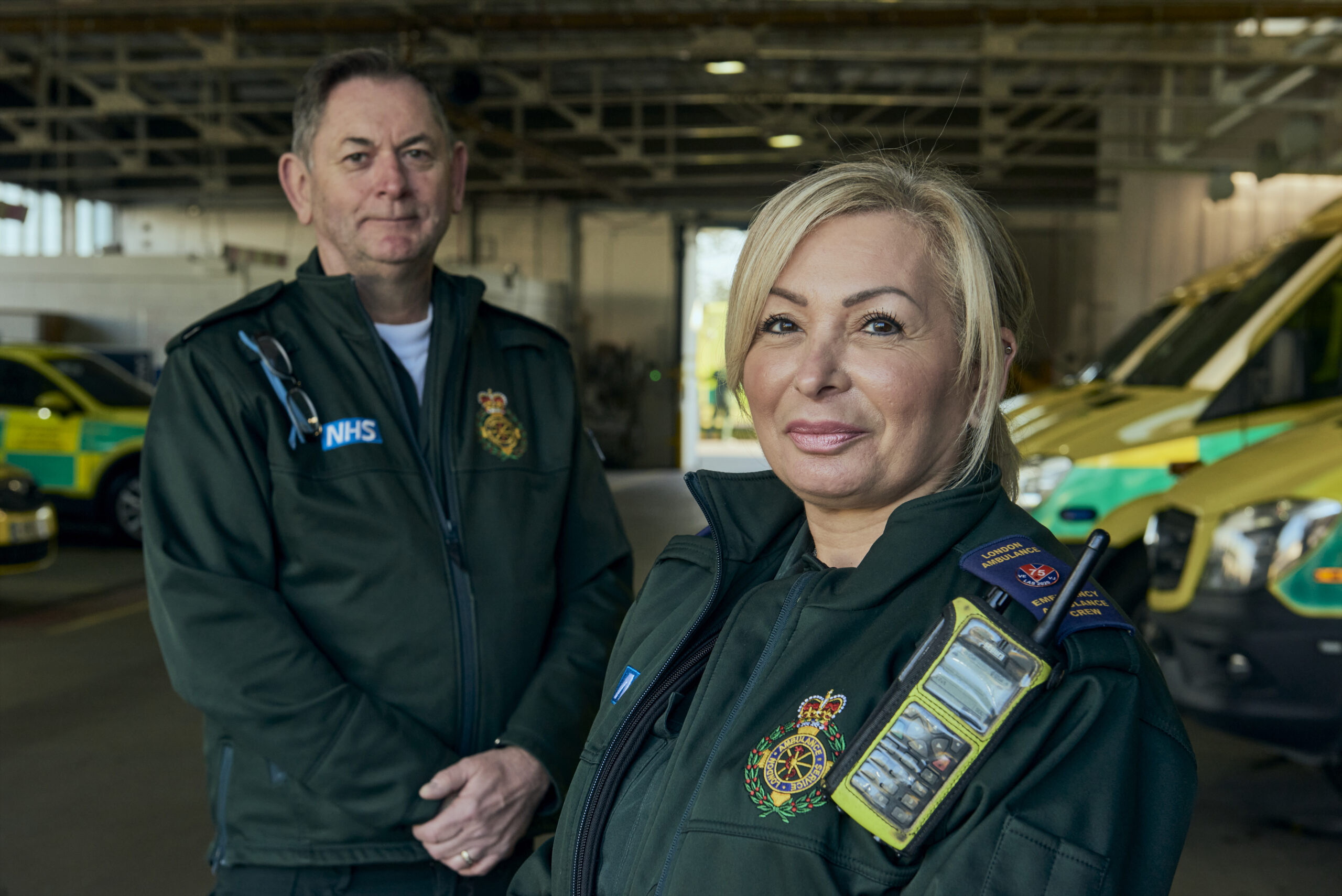 Dave and Ellie stood in LAS uniform in front of a row of ambulances