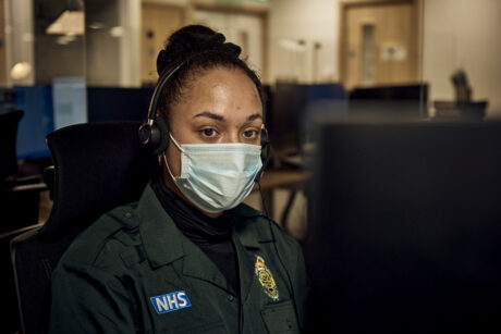 A call handler, wearing a mask and a headset photographed at her workstation