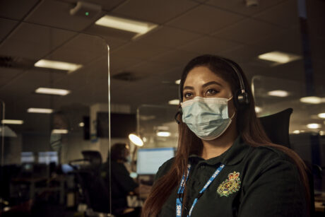 A call handler, wearing a mask and a headset photographed at her workstation