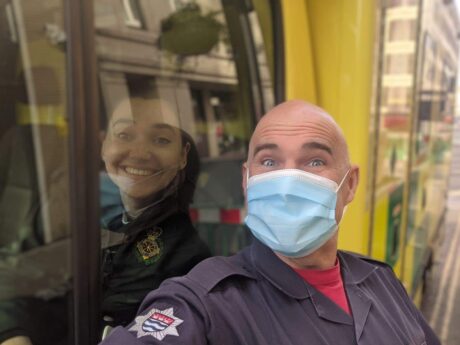 Firefighter Martin stood with a mask next to ambulance cab window with Rebecca shown behind the window glass smiling