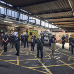 A number of ambulance staff and Chief Midwifery Officer stood in an ambulance garage