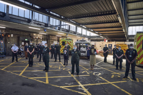 A number of ambulance staff and Chief Midwifery Officer stood in an ambulance garage 