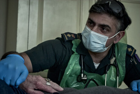 A paramedic with a mask and apron comforting a patient