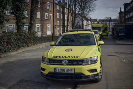 An ambulance car shown parked up in front of another ambulance car and an ambulance on a residential street