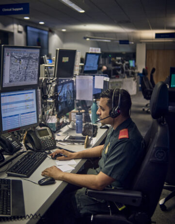 An advanced paramedic in a control room with a headset looking at multiple screens