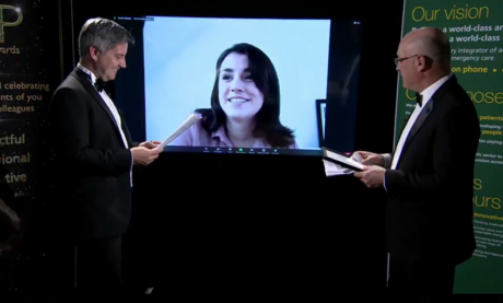 Flavia on a video screen speaking while event presenters stand in foreground