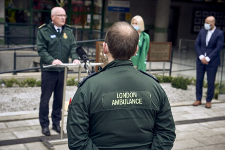 The rear of an ambulance crew's jacket which reads ambulance as he watches a speech being made