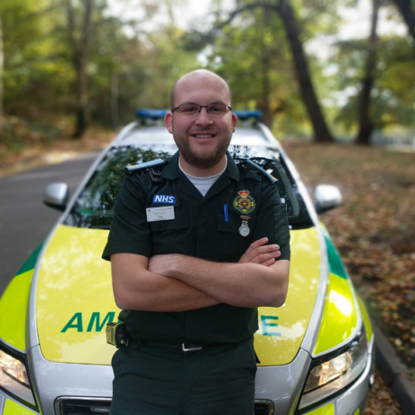 Tyler in LAS uniform arms crossed smiling in front of an ER car