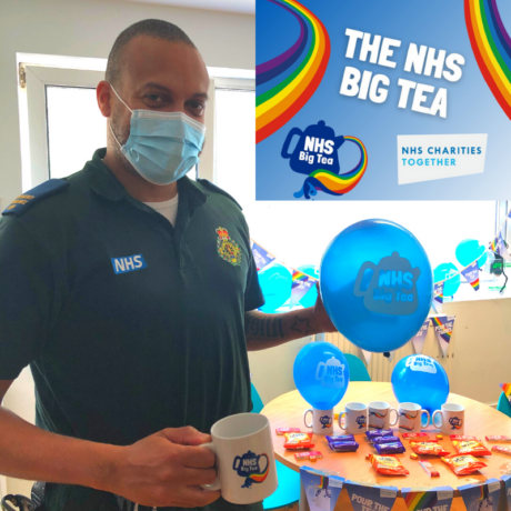 Medic in LAS uniform holds a NHS Big Tea mug and balloon in front of a tea party stall on treats and balloons