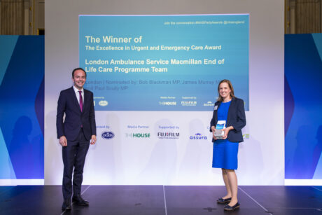 Paramedic Georgina Murphy Jones from the LAS EoLC team alongside James Murray MP on stage holding the team's award