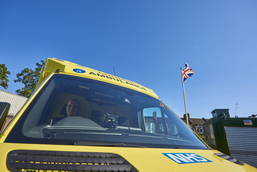 The front cab of an ambulance parked in an ambulance station with sunny blue sky in the background