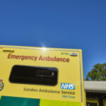 The side of an ambulance parked in an ambulance station with sunny blue sky in the background