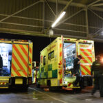 A row of ambulances in an ambulance station from the rear with crews getting kit ready