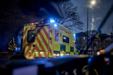 An ambulance with blue flashing lights shown driving from another vehicle following behind's cab